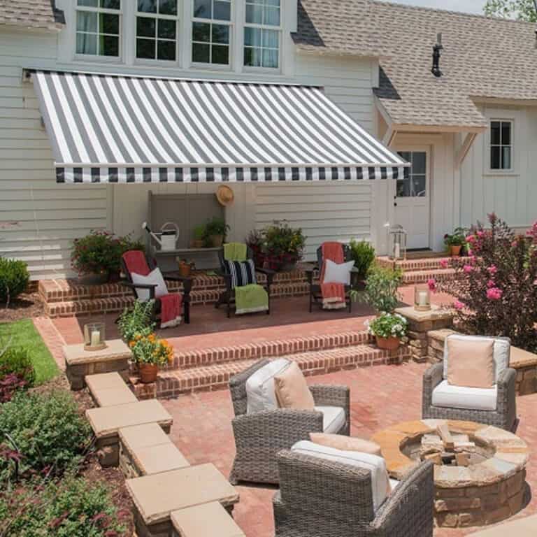 Colorful outdoor patio with striped retractable awning, wicker chairs, and lush garden with blooming flowers for shade and comfort.