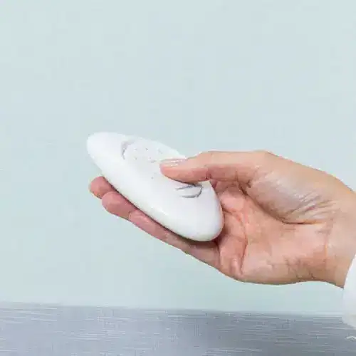 Soft white remote control device held in hand, designed for adjusting window blinds.