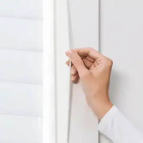 Light control blind cord being adjusted on white window blinds for a modern home interior.