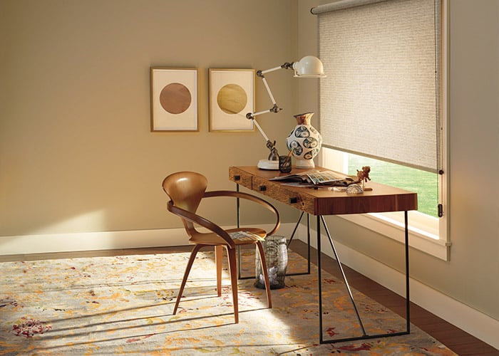Elegant home office with custom roller shades, wooden desk, and modern decor, highlighting stylish window coverings for privacy and light control.