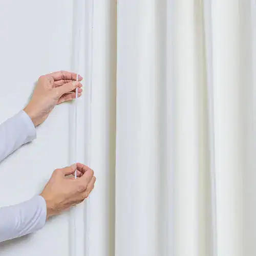 Silhouette of a person installing white custom window blinds in a bright room with white curtains.