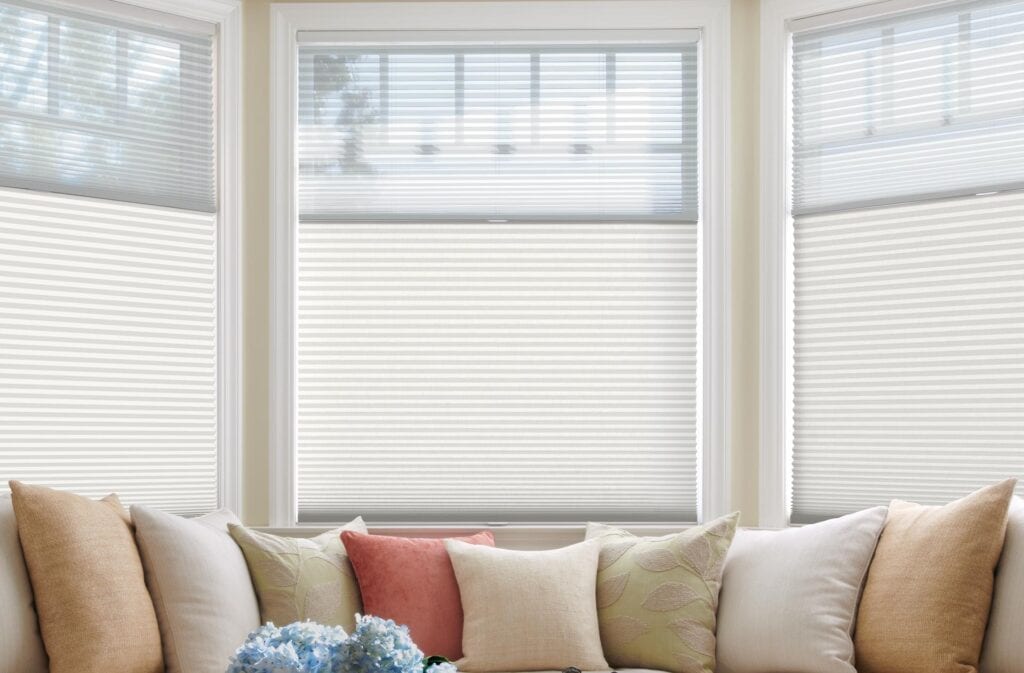 Light filtering white pleated blinds on large windows in a cozy living room with beige and pastel cushions, ideal for privacy and sun control, complementing modern home decor.