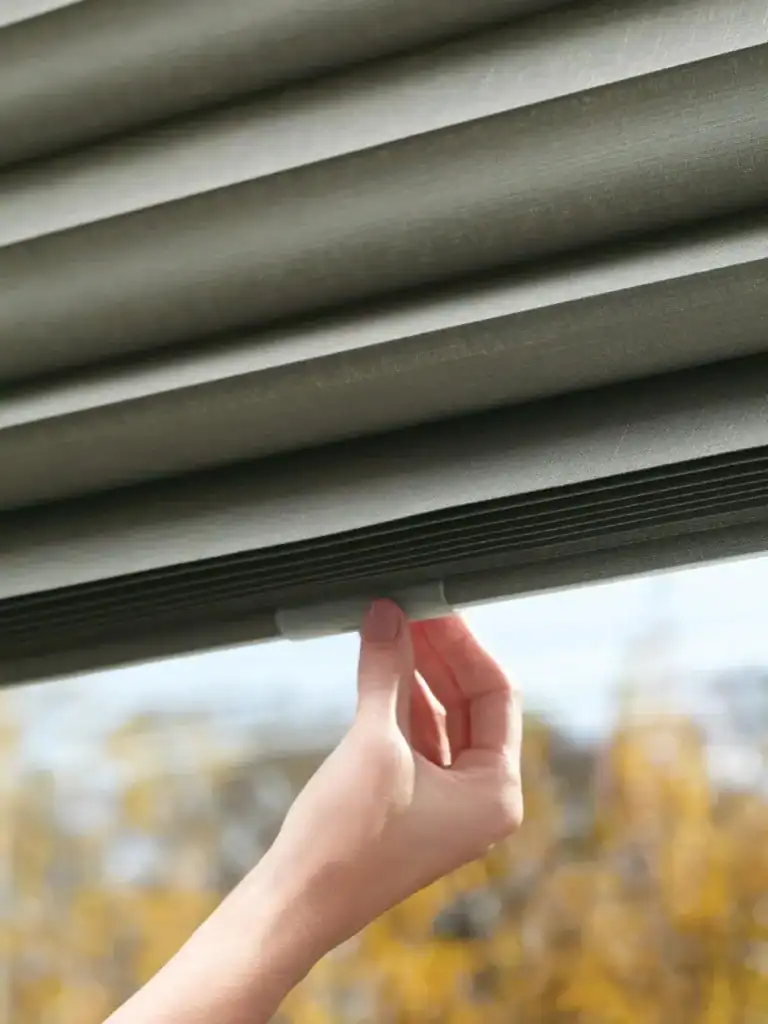 Luxurious gray window blinds with a hand pulling the bottom edge, showcasing sleek and modern window treatment options.