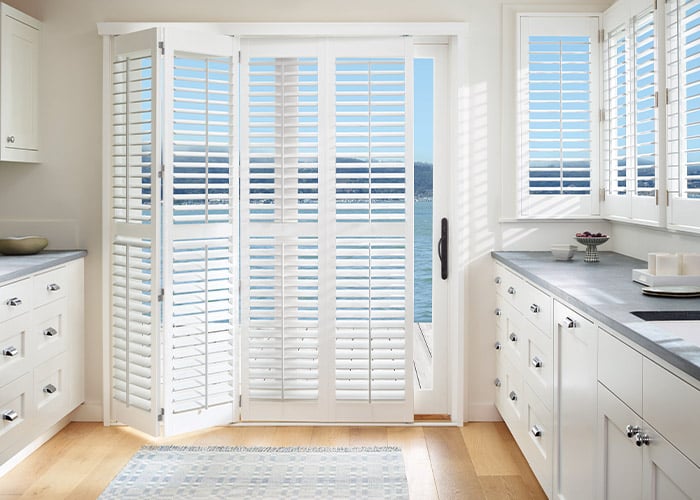 White plantation shutters installed on a sliding glass door in a bright kitchen, offering stylish window coverage and light control. Perfect for enhancing home interiors with superior blinds.
