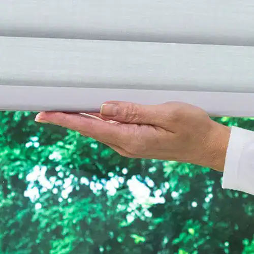 Smooth white window blinds with a person's hand adjusting them, showcasing premium window treatment solutions.
