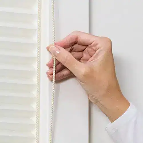 Soft white cord being adjusted on a pair of white blinds, showcasing window covering customization and control.