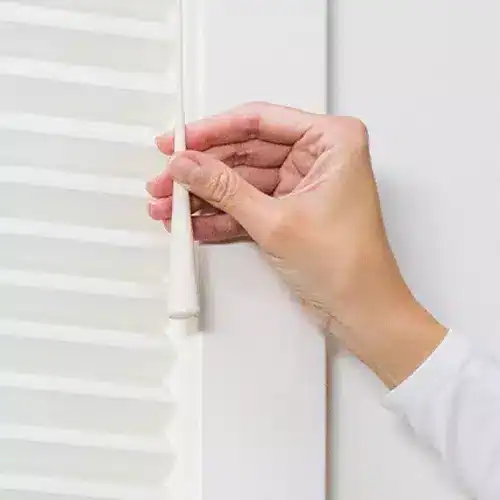 Smooth white window blinds being adjusted with a hand for optimal light control and privacy.
